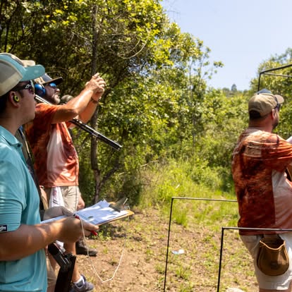 Coach at Gold Valley Gun Club pointing out a target line beside two shooters on the stand