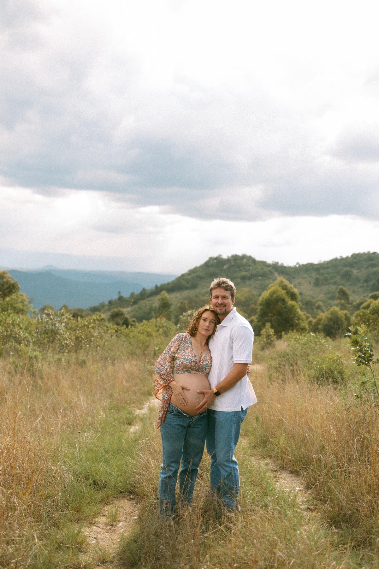 Expecting couple in high grass with mountains behind